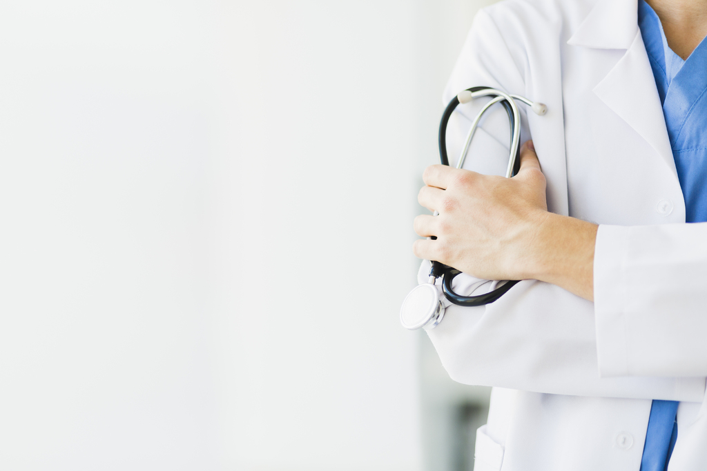 Médecin, vêtue d'une blouse de laboratoire et d'un stéthoscope, photographiée par-dessus son épaule, gérant son cabinet grâce à une assurance professionnelle